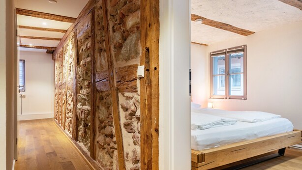 A bedroom with a wooden bed, stone wall, and wooden flooring. - Apartment '2' in Bodman-Ludwigshafen (Bodman-Ludwigshafen)