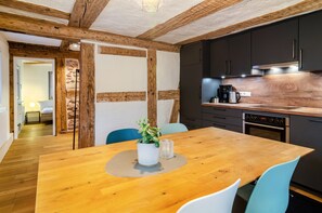 Une cuisine moderne avec des meubles de couleur sombre, un plan de travail en bois et un coin repas comprenant une table et des chaises en bois.