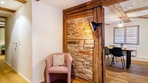 A room with a brick wall, a wooden ceiling, a pink armchair, a dining table with chairs, and a floor lamp. - Apartment '2' in Bodman-Ludwigshafen (Bodman-Ludwigshafen)