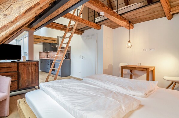 A bedroom with a loft-style ceiling, a wooden desk, a chair, a bed, and a television.