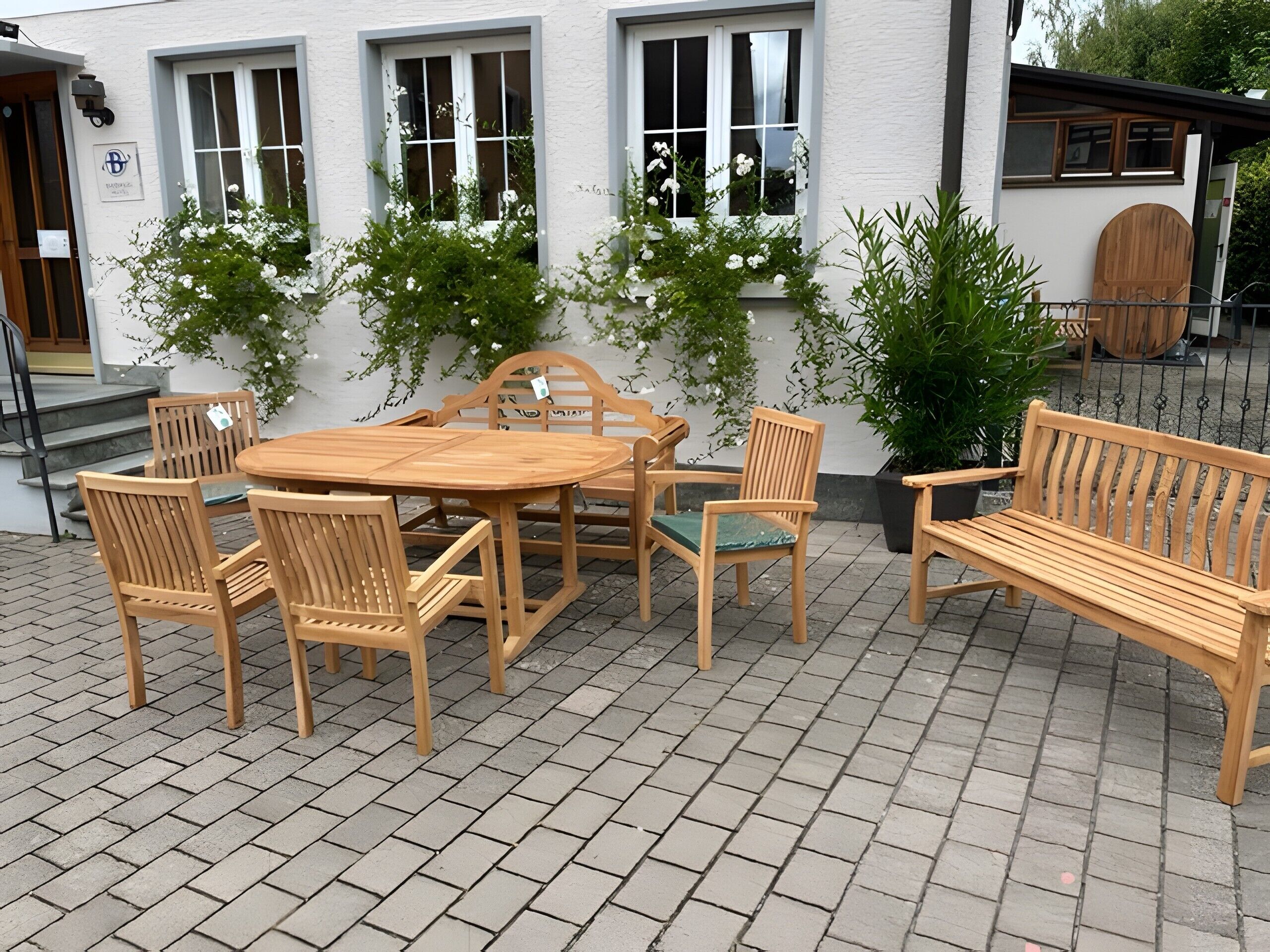 Eine Terrasse im Freien mit einem Holztisch, Stühlen, einer Bank und Topfpflanzen.