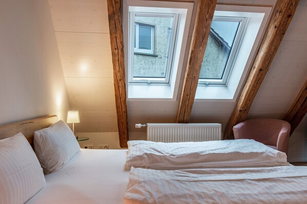 A bedroom with a skylight, a bed, a chair, and a nightstand with a lamp.