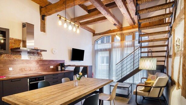 A modern kitchen with a wooden table, black chairs, a TV, and a staircase leading to a balcony. - 'Family Apartment 6' (Bodman-Ludwigshafen)