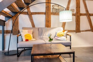 A cozy room with a wooden ceiling, a sofa with cushions, a table, and a lamp.