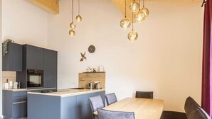 Una cocina moderna con una isla central, armarios oscuros y una mesa de comedor de madera con sillas tapizadas en gris.