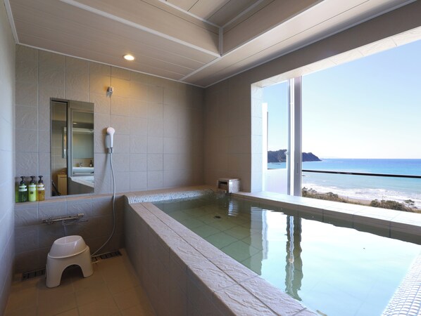 Un baño moderno con una bañera grande, un inodoro y una ducha. Cuenta con un ventanal con vistas al océano.