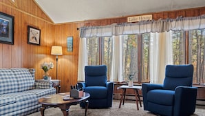 Una sala de estar acogedora con un sofá azul, dos sillones azules, una mesa de centro y vistas a árboles a través de amplias ventanas.