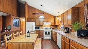 Una cocina de madera con una mesa de comedor, sillas, un refrigerador, microondas, horno y una cafetera.