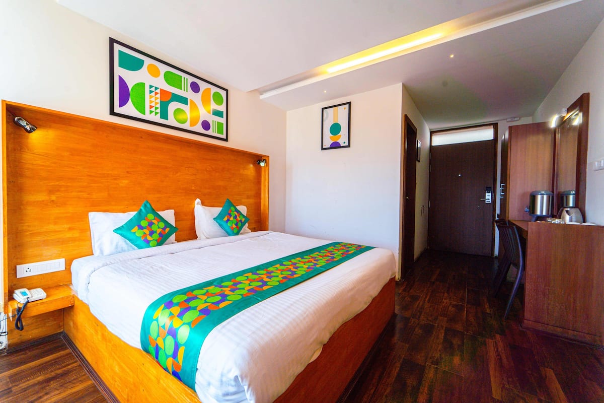 Quarto de hotel com uma cama grande, cabeceira de madeira, obras de arte coloridas, uma escrivaninha com cadeira e um guarda-roupa.