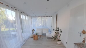 Amplia sala de estar con piso de madera, un sofá blanco, una mesa redonda y una planta en maceta.