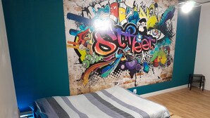 Un dormitorio con una cama, un mural en la pared y una mesita.