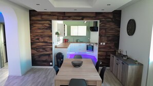 Una cocina moderna con salpicadero de pared de piedra, un comedor con mesa y sillas de madera, y una vista hacia la cocina a través de un arco.