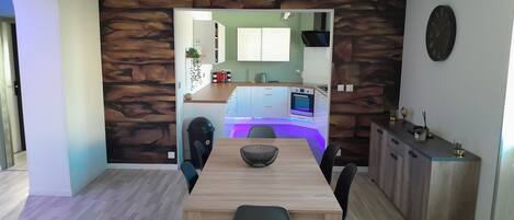 Una cocina moderna con salpicadero de pared de piedra, un comedor con mesa y sillas de madera, y una vista hacia la cocina a través de un arco.