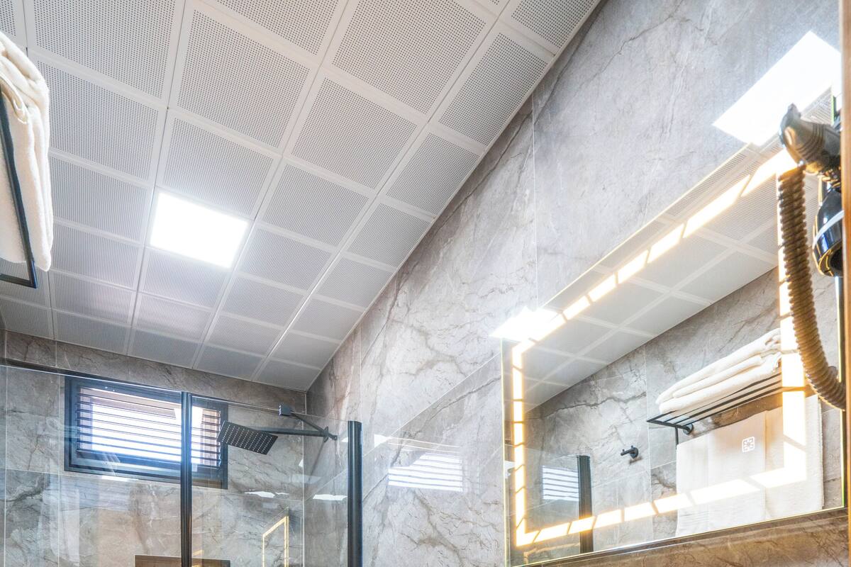 A modern bathroom with a glass-enclosed shower, a white sink, and a large mirror with integrated lighting.