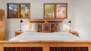 Une chambre avec un lit en bois, deux tables de chevet avec des lampes, une fenêtre donnant sur des arbres et un plafond en bois.