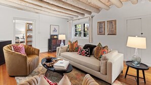 Un salon comprenant un canapé, un fauteuil et une table basse. On y trouve également deux lampes, une bibliothèque et une porte qui donne sur une autre pièce.