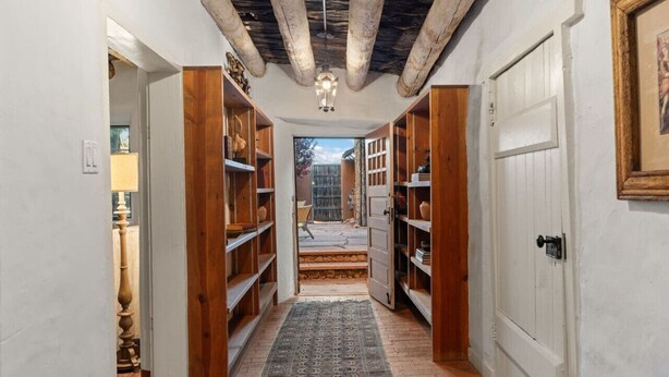 Un couloir étroit avec des étagères en bois remplies de livres, un tapis à motifs et un plafond avec des poutres apparentes.