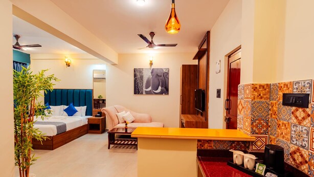Habitación de hotel con cama, sofá, una mesita, una planta, ventilador de techo, televisor montado en la pared y salpicadero de azulejos.