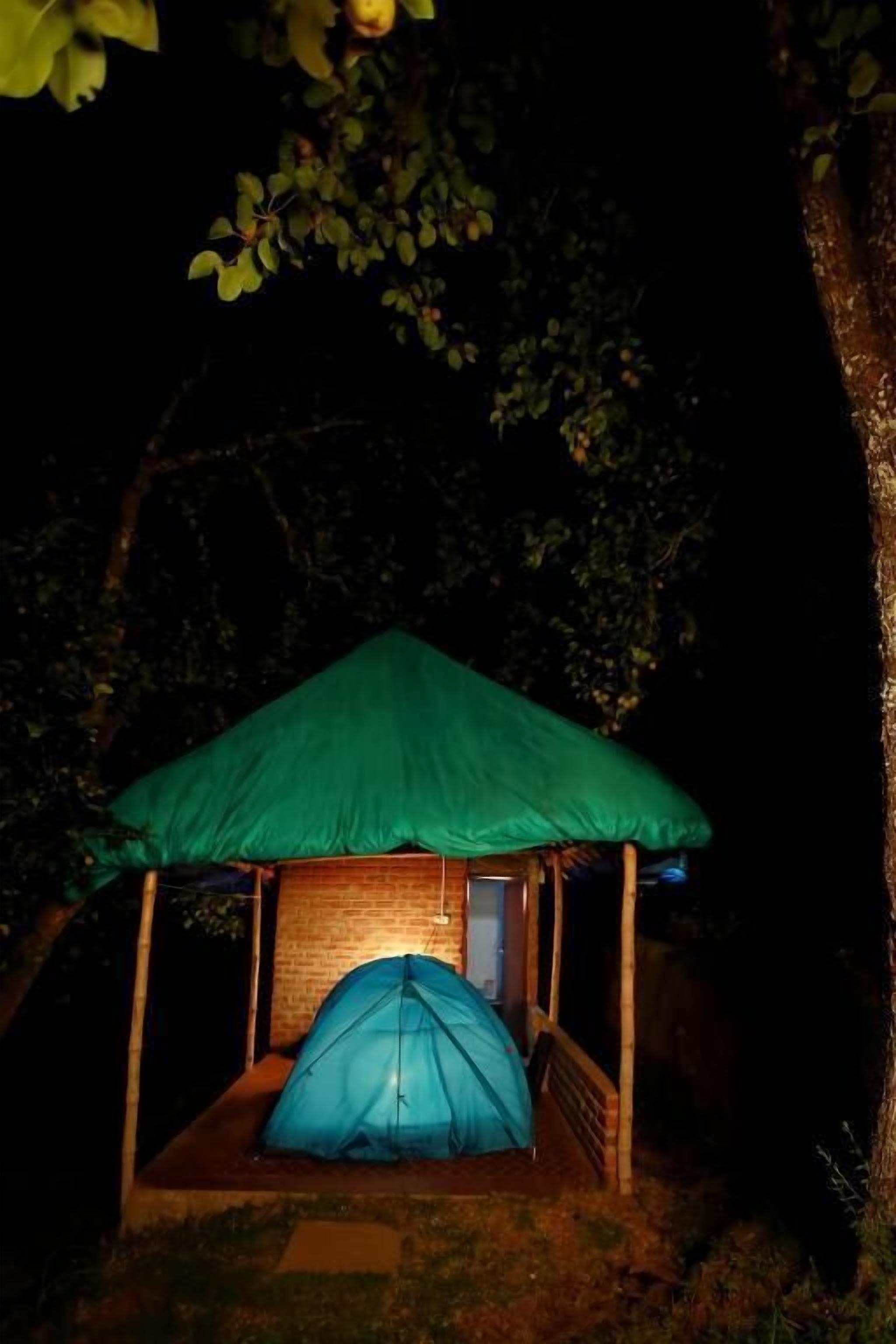 A small, single-room structure with a green roof and a blue tent-like enclosure.