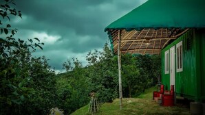 Un bâtiment écologique doté d’une toiture en chaume, entouré d’une végétation luxuriante et surplombé d’un ciel nuageux.