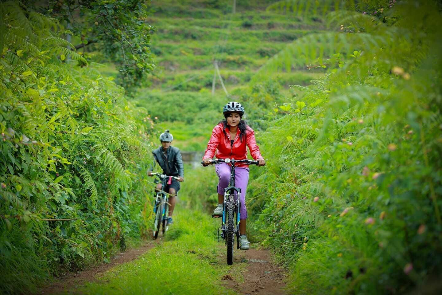 Two cyclists on a dirt path surrounded by lush greenery.