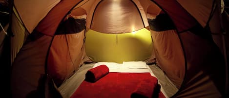 A tent with a bed, a red blanket, and a single light bulb.