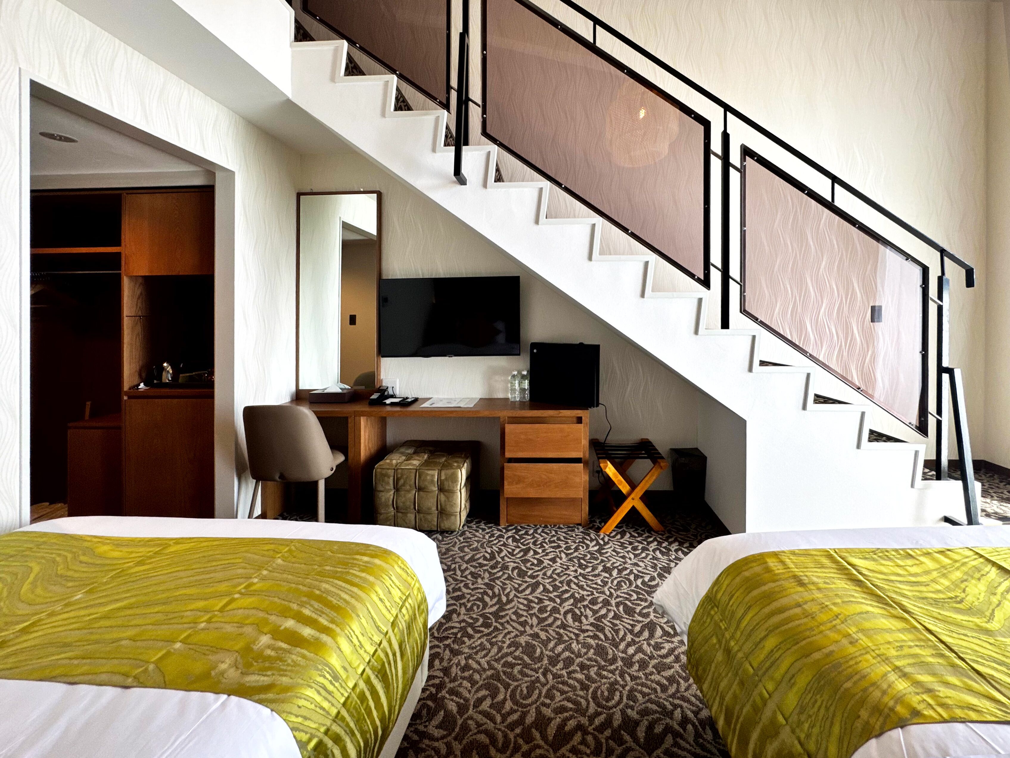 Ein Hotelzimmer mit zwei Betten, einem Schreibtisch, einem Sessel, einem Fernseher und einer Treppe.