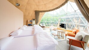 Ein geräumiges Zimmer mit großem Fenster, Deckenventilator und einer Sitzecke mit Tisch und Stühlen.