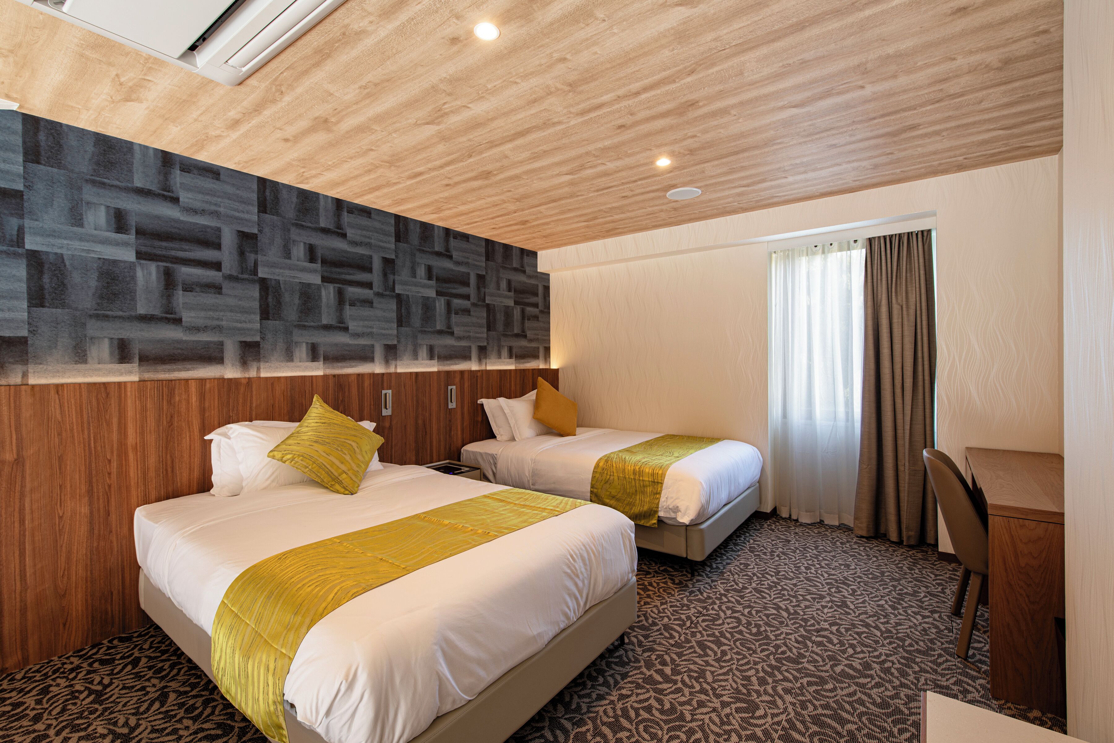A hotel room with two beds, a desk, and a patterned carpet.