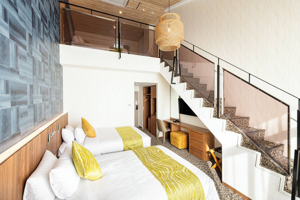 A modern hotel room with a large bed, a desk, a chair, and a staircase.