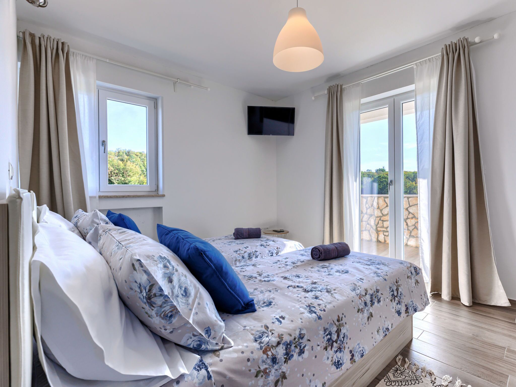 Quarto com cama, cortinas, televisão e varanda.