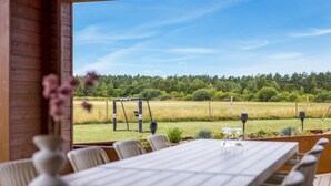 A dining area with a long table and chairs, a view of a grassy field and trees, and a wooden interior. - "Sönke" - 4km from the sea by Interhome (Rømø)