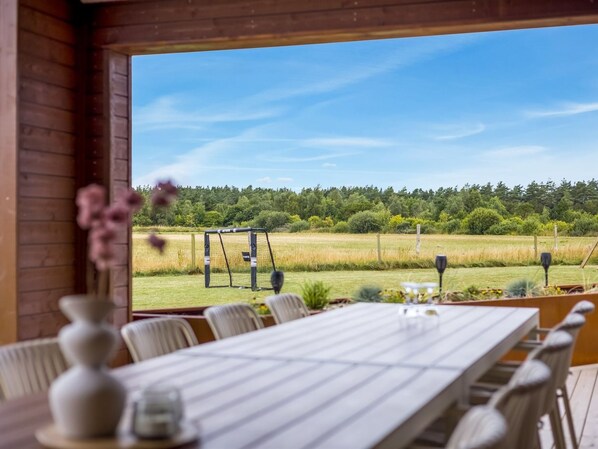 A dining area with a long table and chairs, a view of a grassy field and trees, and a wooden interior. - "Sönke" - 4km from the sea by Interhome (Rømø)