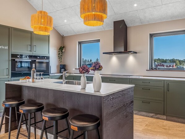 Une cuisine moderne dotée d’un îlot central, de tabourets de bar et de luminaires suspendus.
