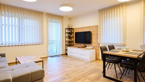 A modern living room with a sofa, a dining table with chairs, a TV mounted on the wall, and a wooden cabinet. - Markéta by Interhome (Smržovka)