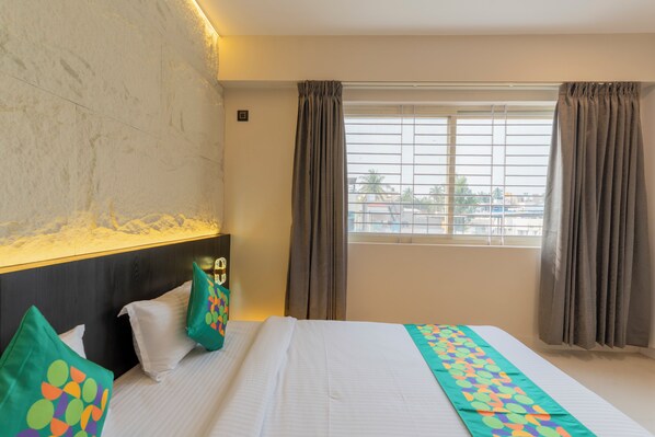 A hotel room with a large bed, a headboard, a window with curtains, and a view of the outside.