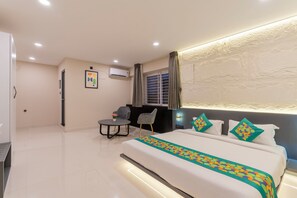 A hotel room with a large bed, a small round table, two chairs, a window with curtains, and an air conditioning unit on the wall. - Treebo Sanmaya Retreat, Mysore (Mysore)