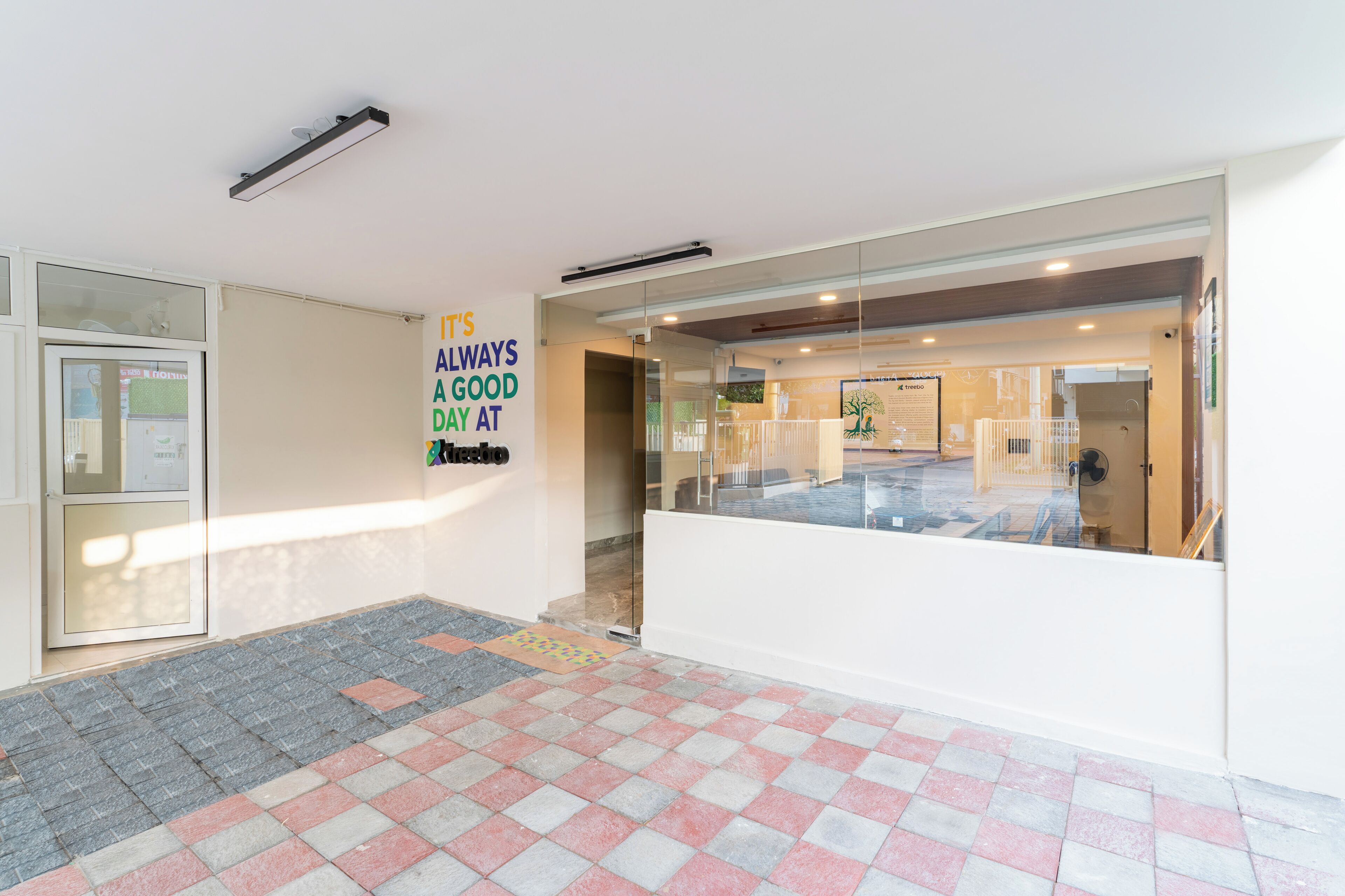 A hotel reception area with a glass partition, a sign that says "It's always a good day at," and a tiled floor.