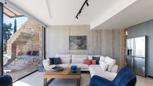 Een moderne woonkamer met een stenen muur, een witte bank, blauwe stoelen, een salontafel en een keuken met een koelkast.