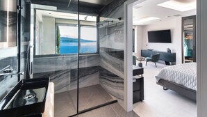 A modern bedroom with a large bed, a TV, and a view of the sea through a glass door. - Ionian Grand Villas - Villa Naya (QPM9+9JR, Lefkada)
