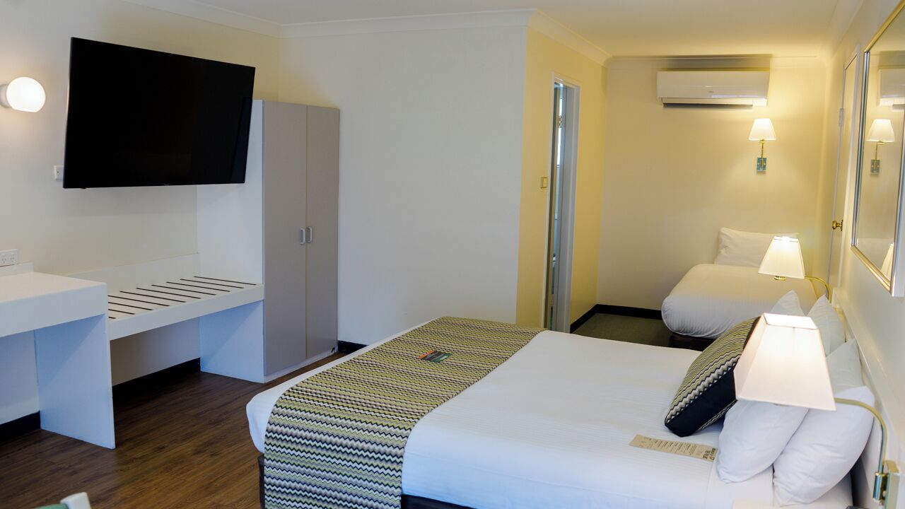 Habitación de hotel con cama, lámparas de noche, televisor montado en la pared, armario y unidad de aire acondicionado.