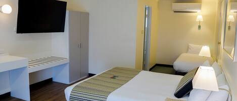 Habitación de hotel con cama, lámparas de noche, televisor montado en la pared, armario y unidad de aire acondicionado.