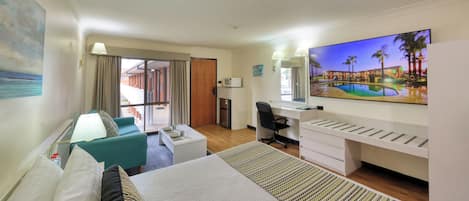A hotel room with a bed, a desk, a chair, a TV, and a balcony with a view of the pool.