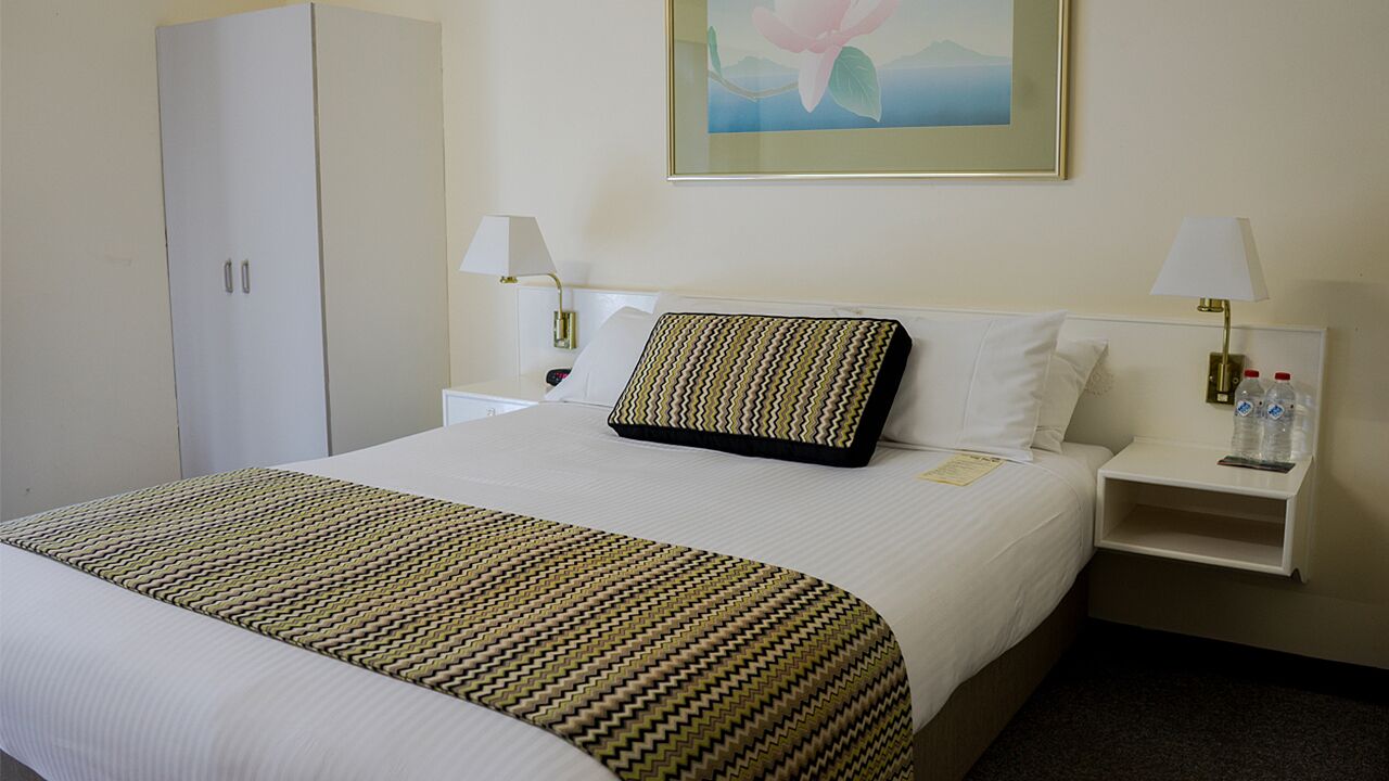 A hotel room with a large bed, two bedside tables, a wardrobe, and a painting on the wall.