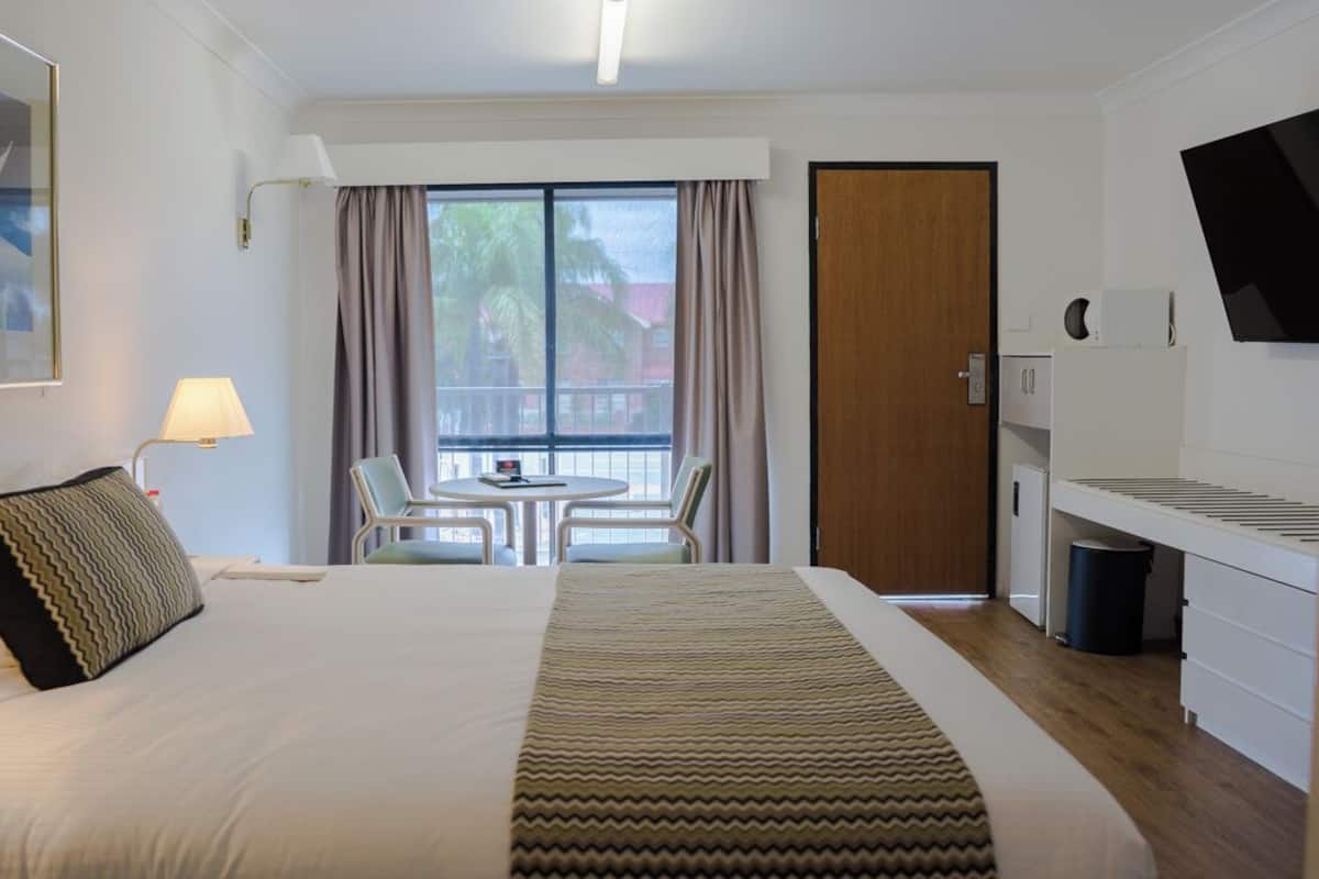A hotel room with a bed, a desk, a chair, a TV, and a window with curtains.