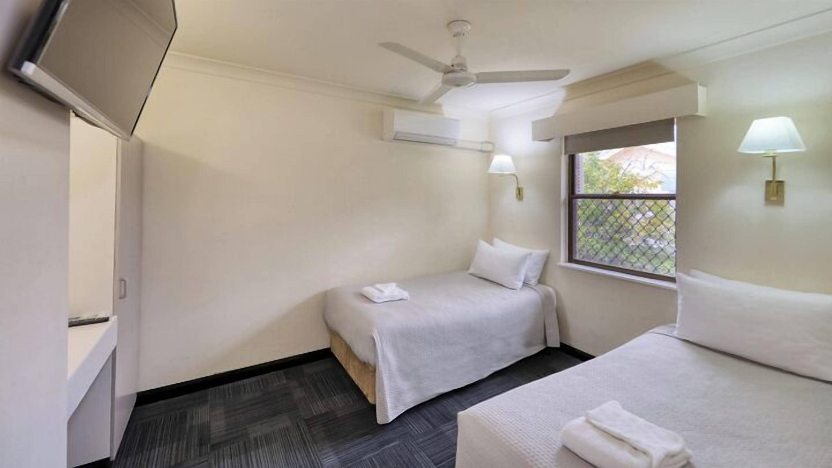 A small, clean room with two beds, a ceiling fan, a window with a view, and a TV on the wall.