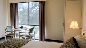 Une chambre d’hôtel avec un lit, un bureau avec deux chaises, une lampe et une fenêtre avec des rideaux.