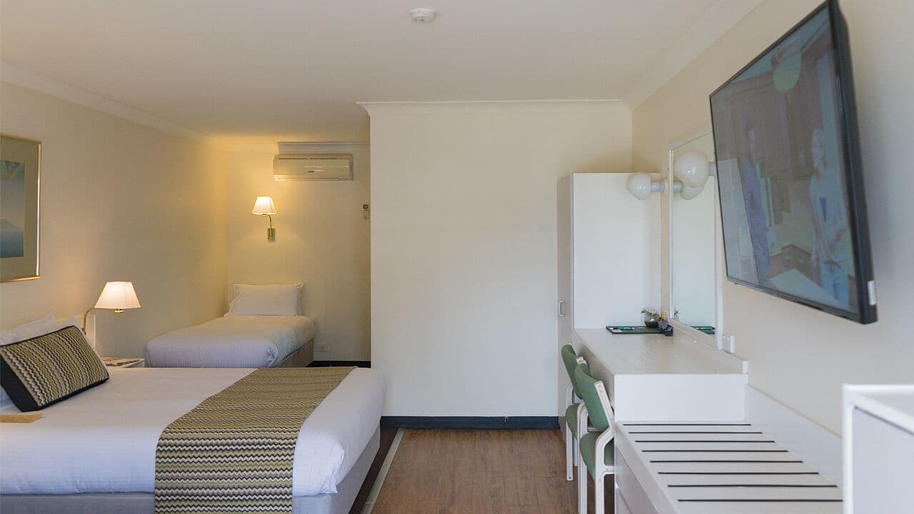 A hotel room with two beds, a desk with a chair, a mirror, and a painting on the wall.