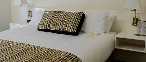 A hotel room with a neatly made bed, two bedside tables with lamps, a framed picture on the wall, and a water bottle on the nightstand.