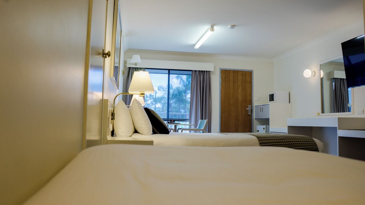 Une chambre d’hôtel équipée d’un lit, d’un bureau, d’une chaise, d’une lampe, d’un téléviseur et d’une fenêtre avec des rideaux.
